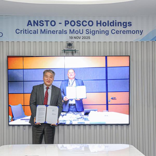 Posco representative stands in front of screen showing ANSTO representative during MOU signing ceremony